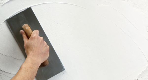 Hand with trowel plastering a white wall